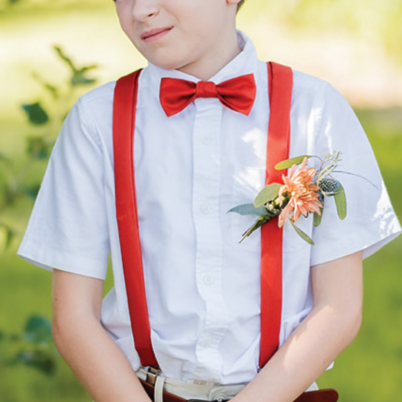 boy wearing red suspenders and bow tie in an outdoor setting 