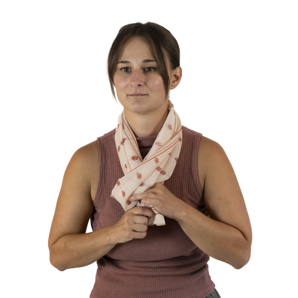 A woman wearing a cream rectangle scarf around her neck, pulling the ends through the scarf loop
