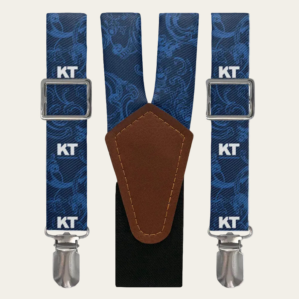 Blue patterned suspenders with brown leather patch and silver clips on a white background