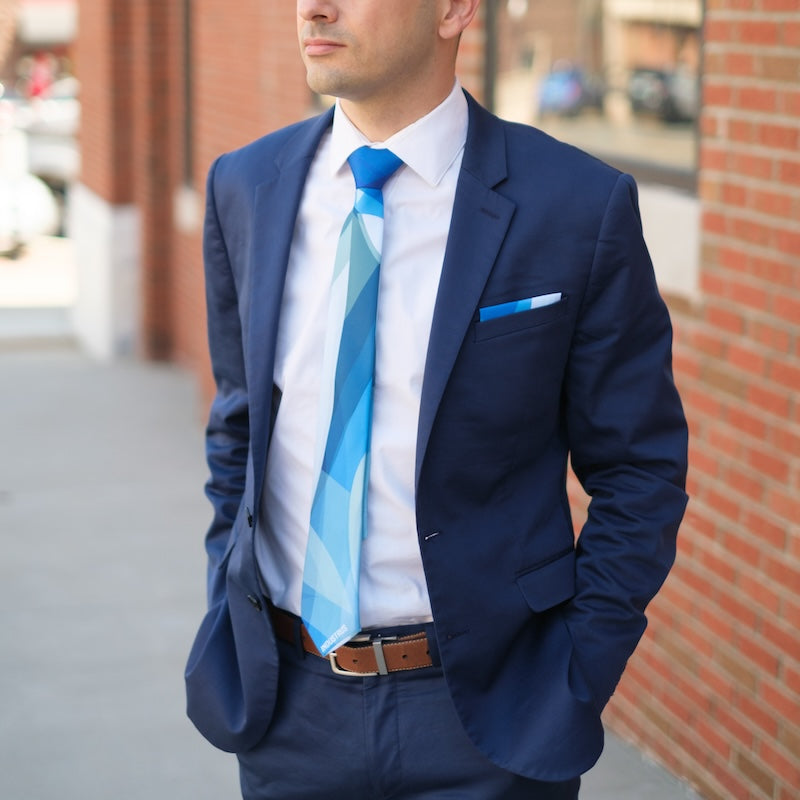 Man in a navy suit with a blue tie standing against a brick wall.