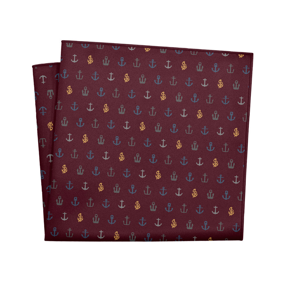 A folded pocket square with a pattern of anchors in blue and gold on a red background.
