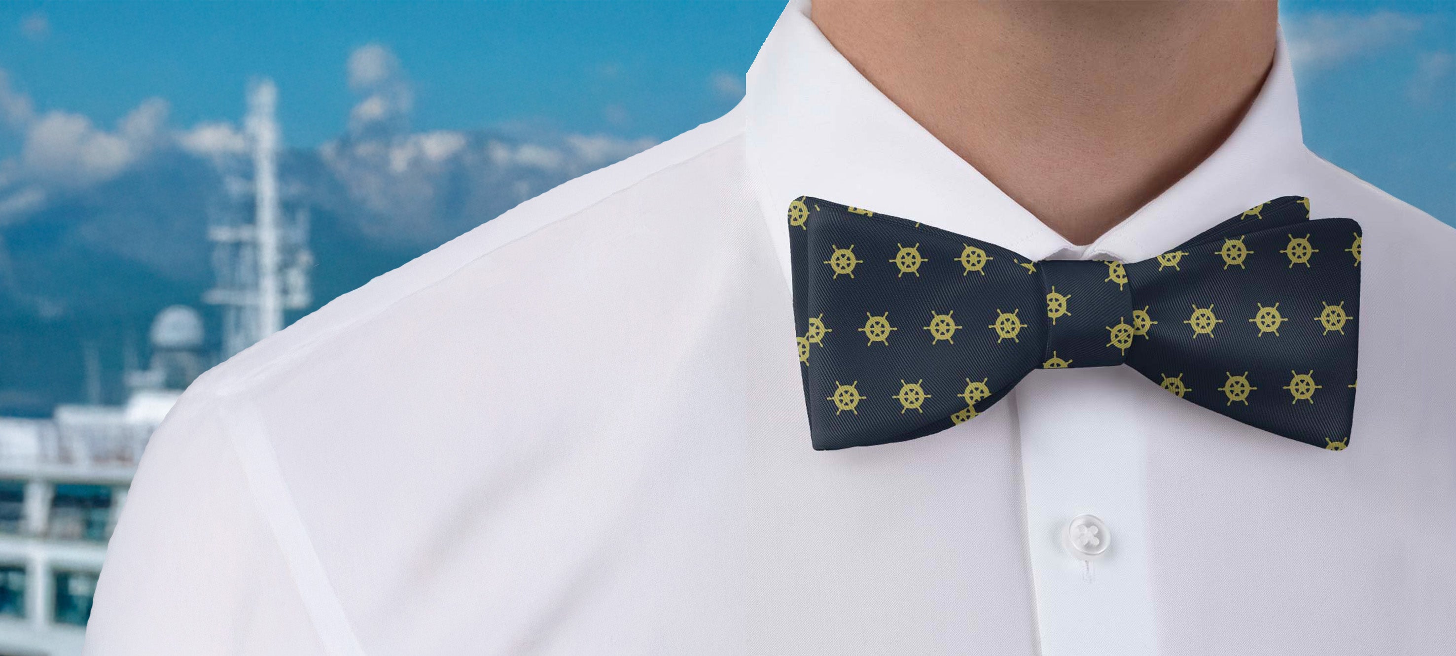 Navy blue nautical bow tie with yellow captain's wheel icons on a white shirt against a blurred background
