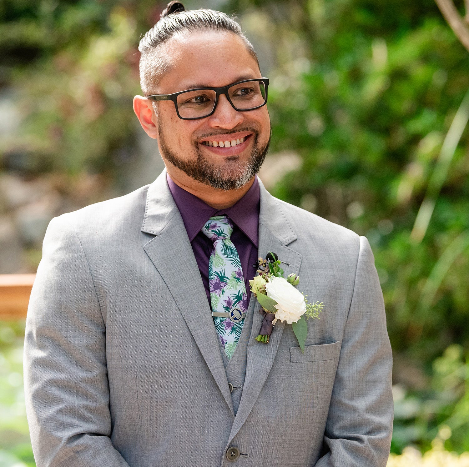 Groom wearing tropical floral necktie smiling with black rimmed glasses
