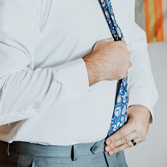 Person adjusting a floral tie on a light gray shirt with a blurred background