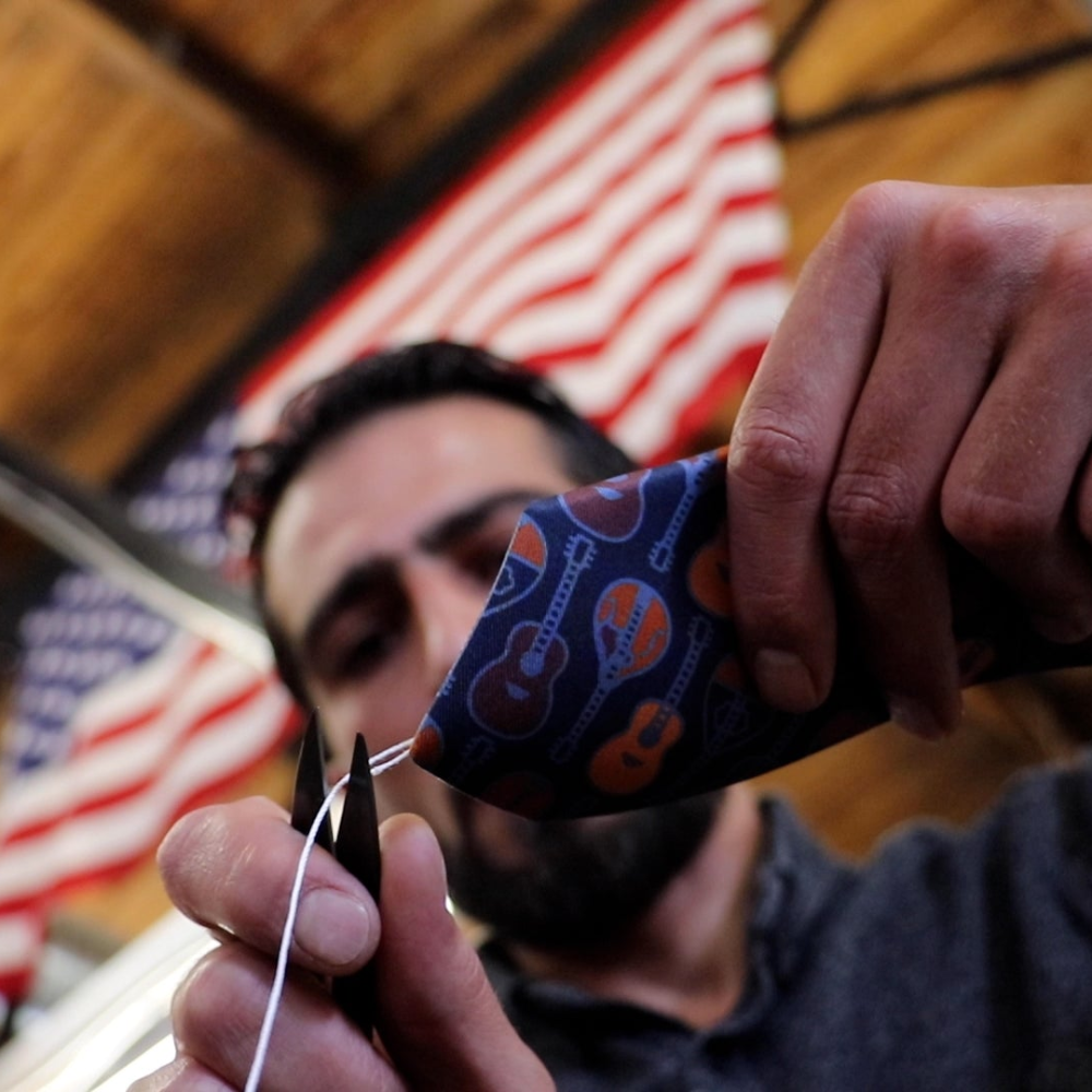 Person holding a blue patterned tie with scissors in front of an American flag