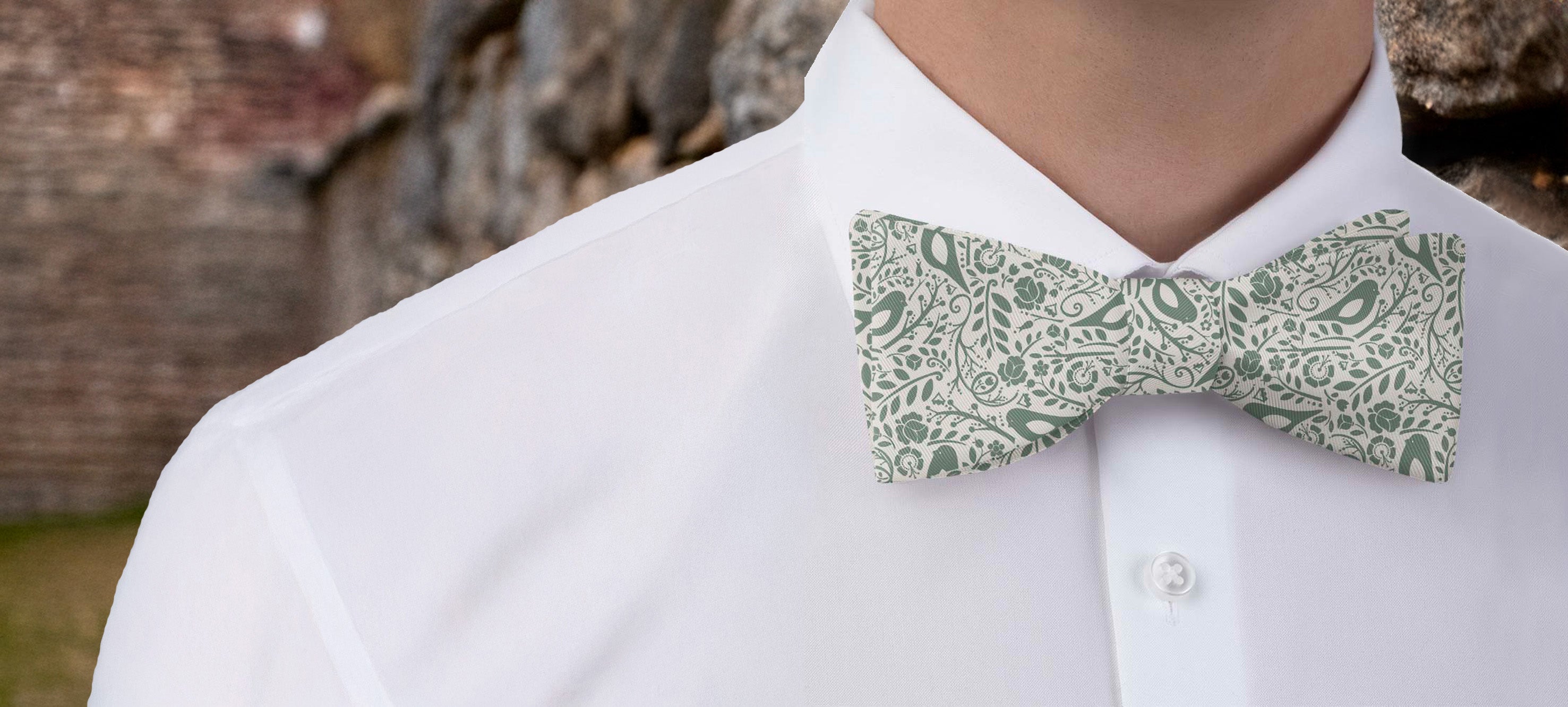 Person wearing a white shirt with an ornate green patterned bow tie against a stone wall background