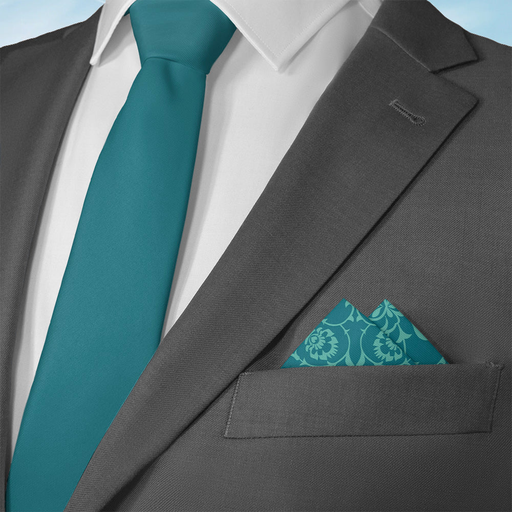 Gray suit with teal tie and ornate pattern pocket square on a light blue background