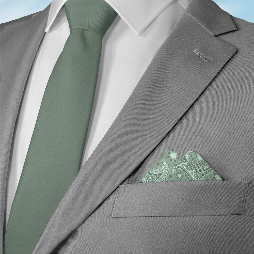 Gray suit with green tie and paisley pocket square on a light blue background