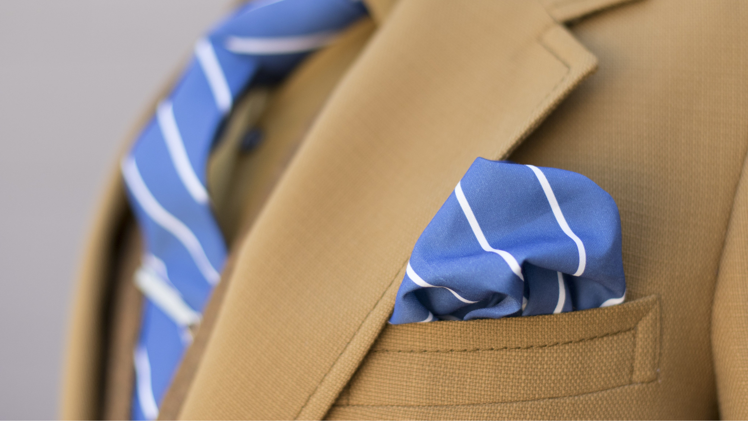 Close-up of a brown blazer with a blue striped tie and pocket square.