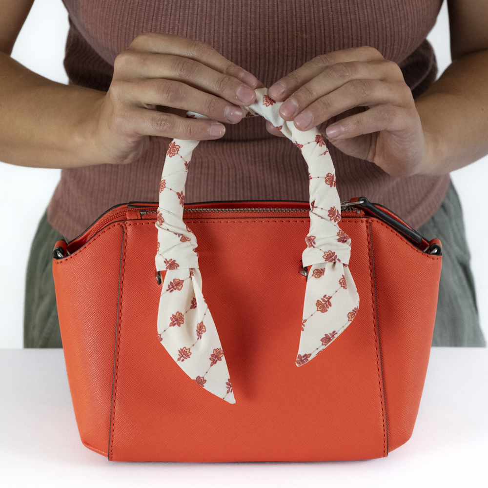 An orange handbag with a cream hair scarf wrapped around the handle.