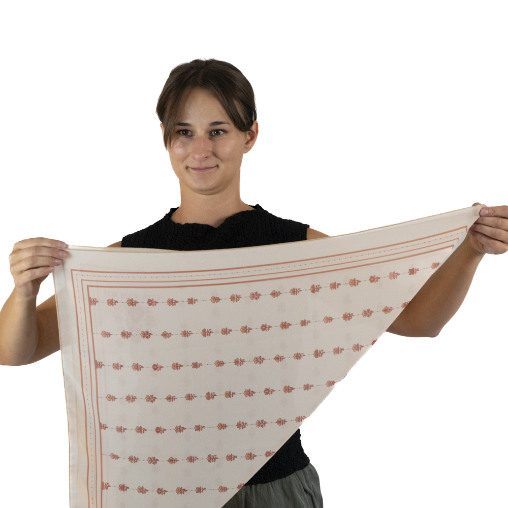 A woman holding up a square cream-colored scarf and folding it into a triangle