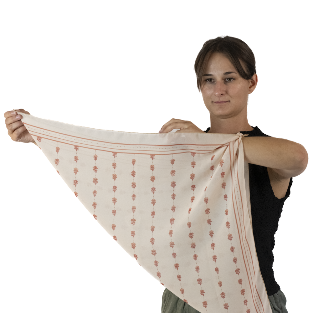 A woman holding up a square scarf with the tied end over her left wrist