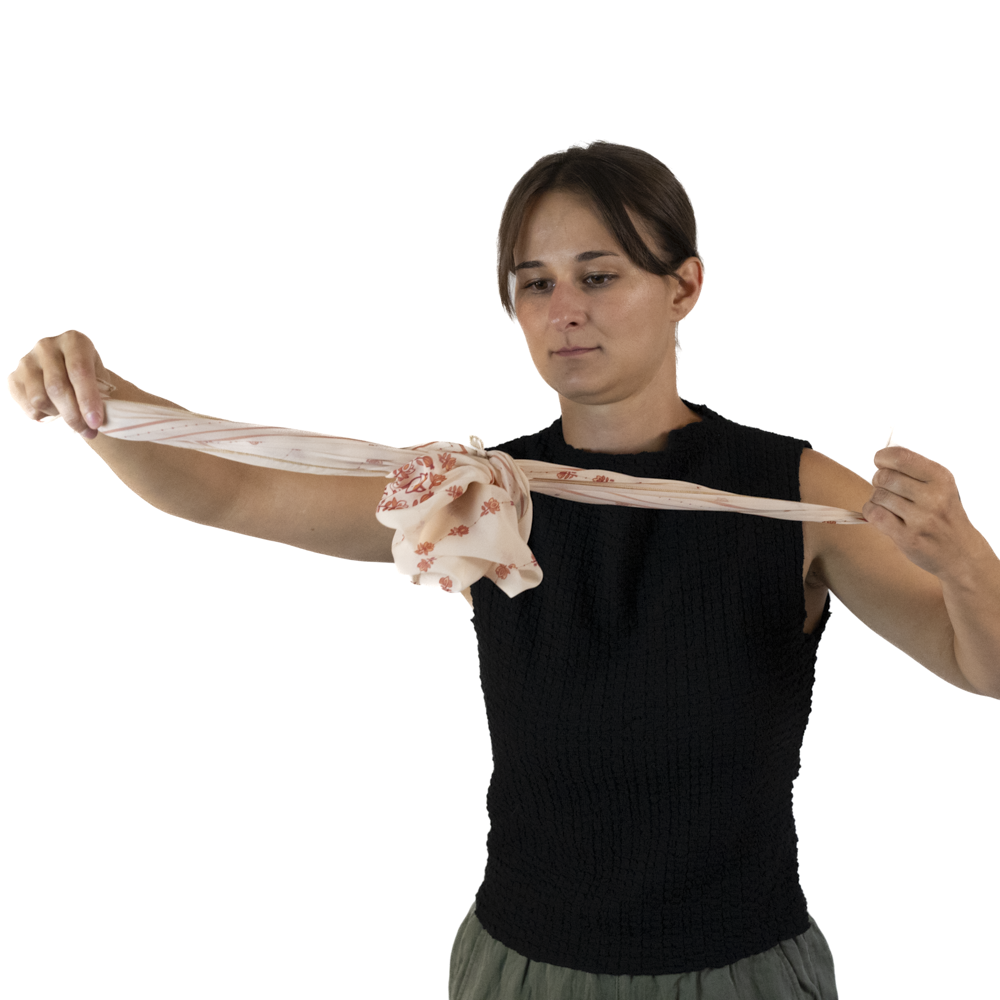 A woman demonstrates how pull the two corners of the scarf to create a rose shape.