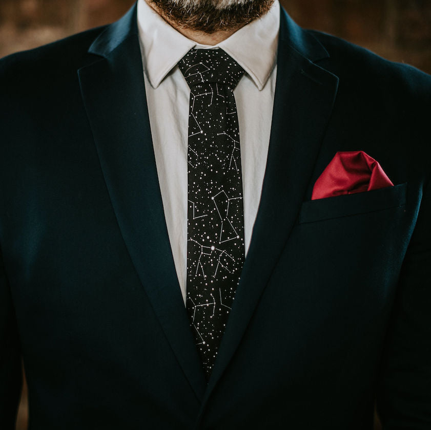 Man wearing a dark suit with a star-patterned tie and red pocket square.