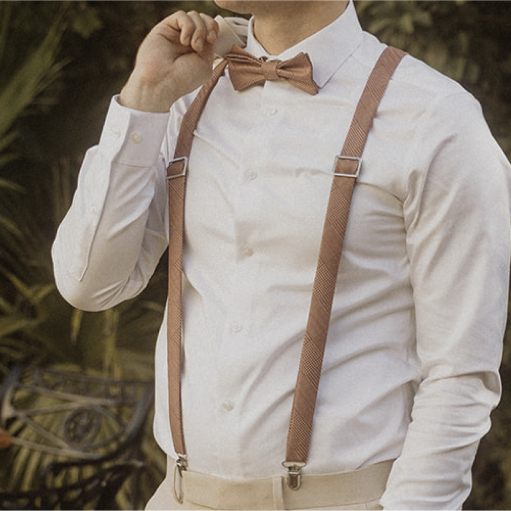 Person wearing a white shirt with brown suspenders and bow tie against a blurred natural background
