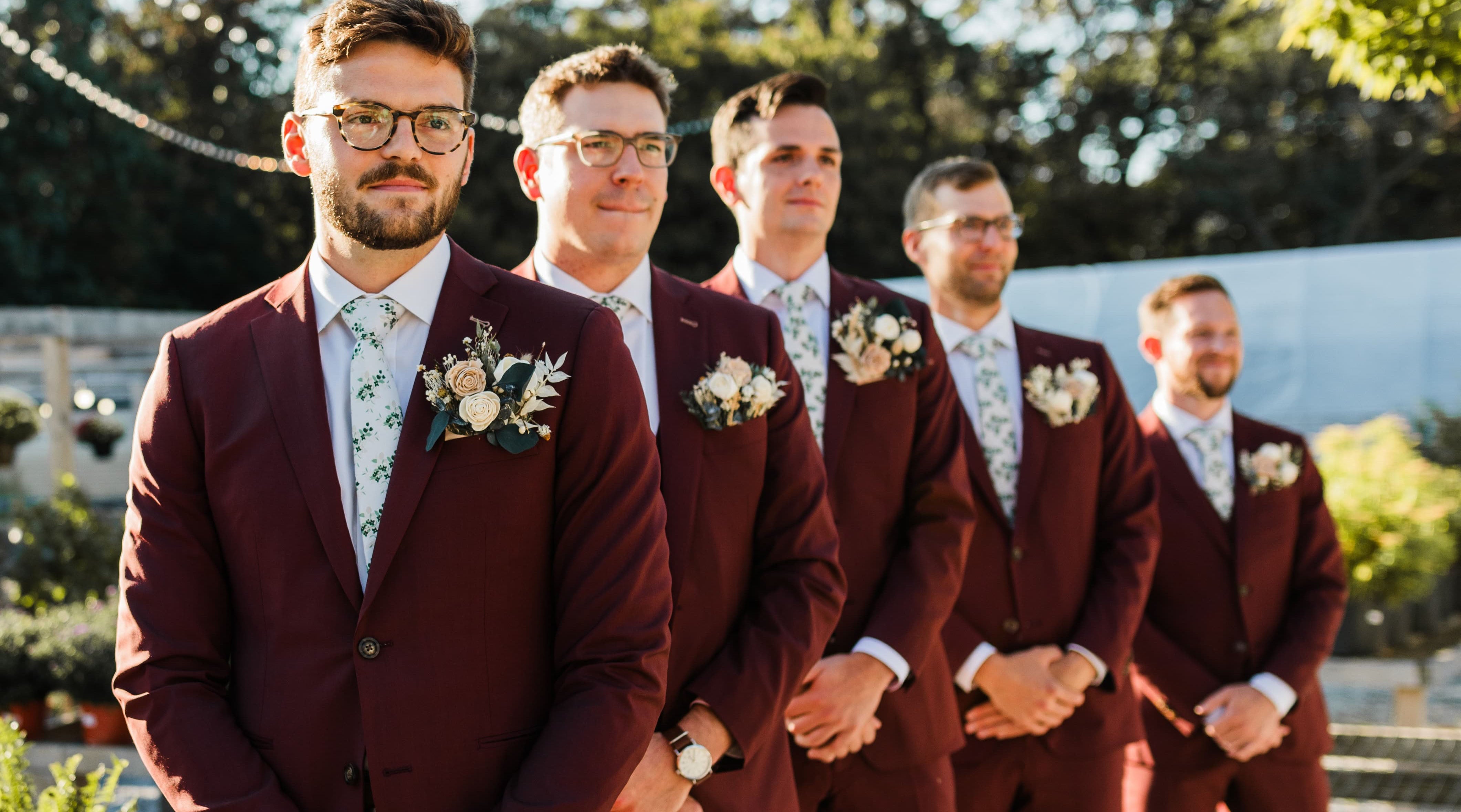 Groomsmen in floral ties and maroon suits lined up at the altar 
