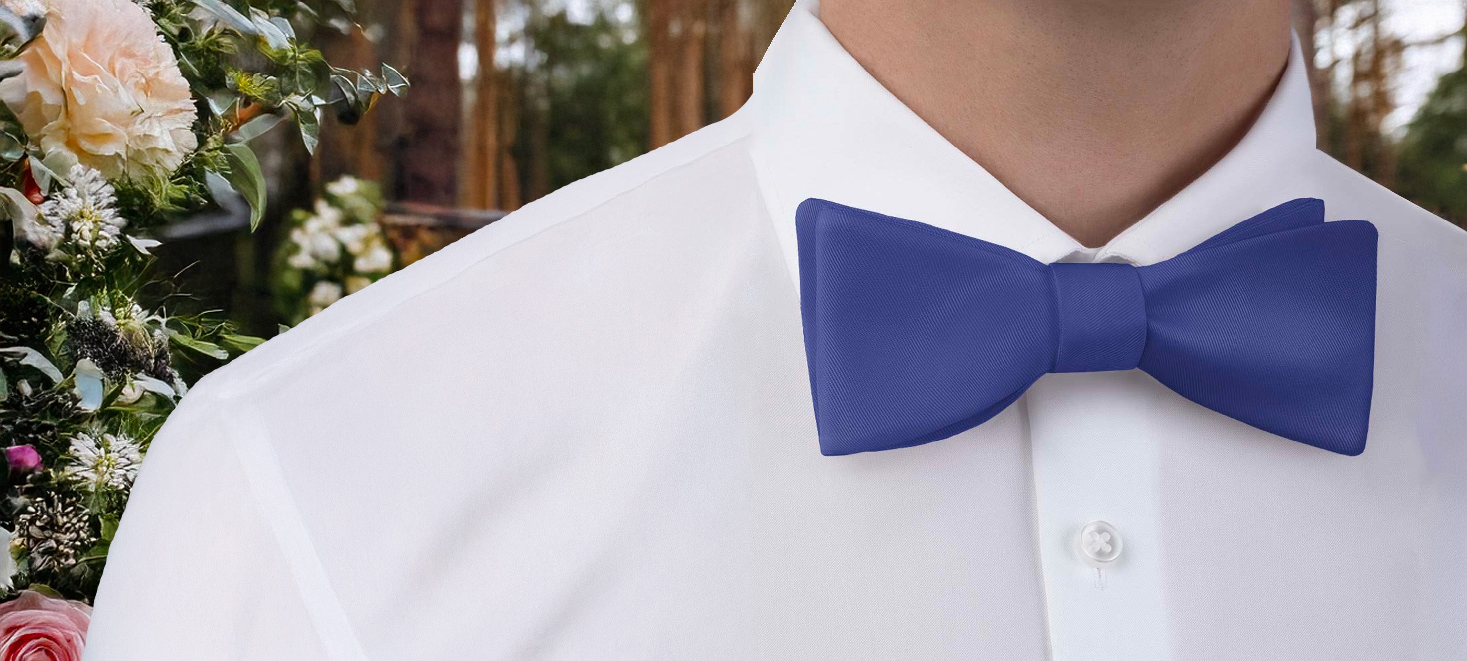 Person wearing a solid blue bow tie with a blurred floral background