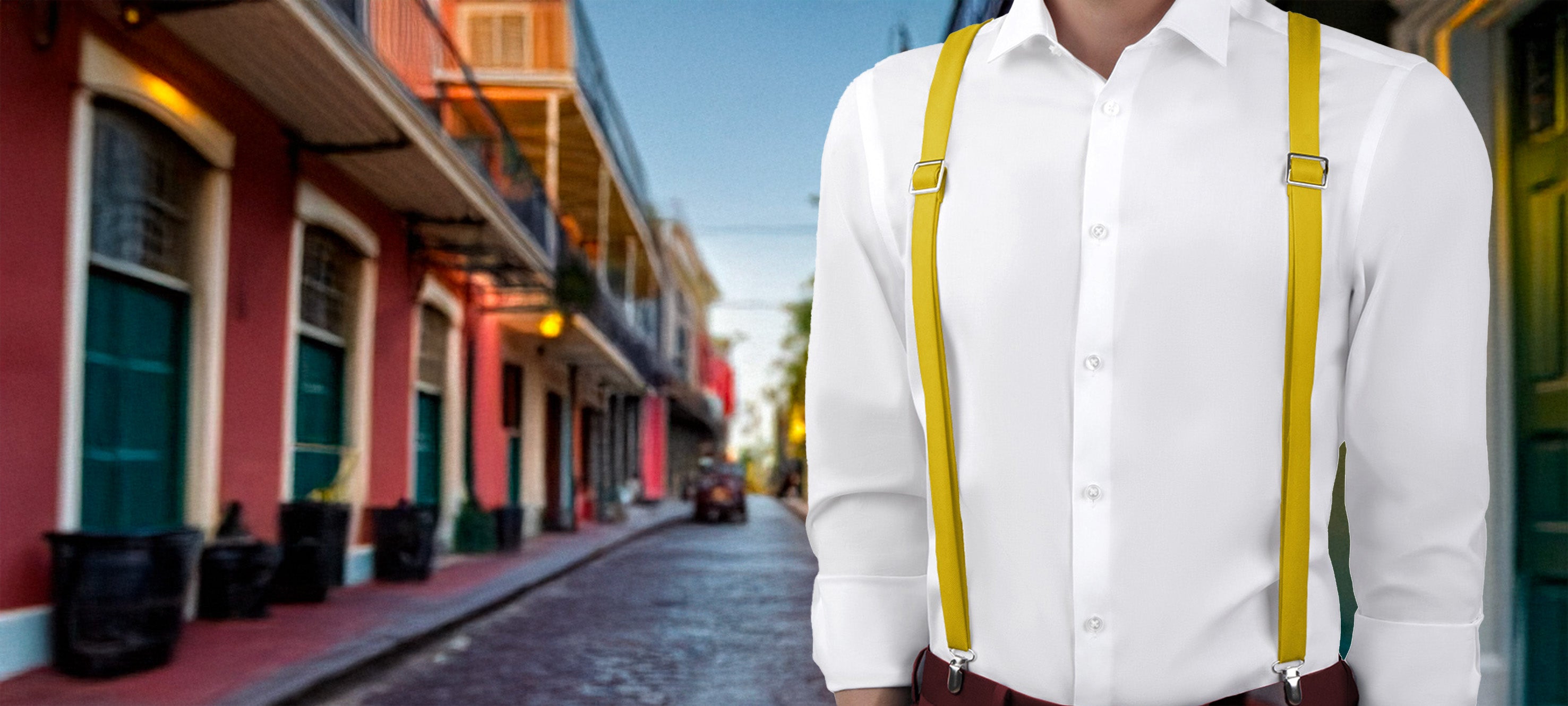 Person wearing a white shirt and yellow solid color suspenders standing on a street with colorful buildings.