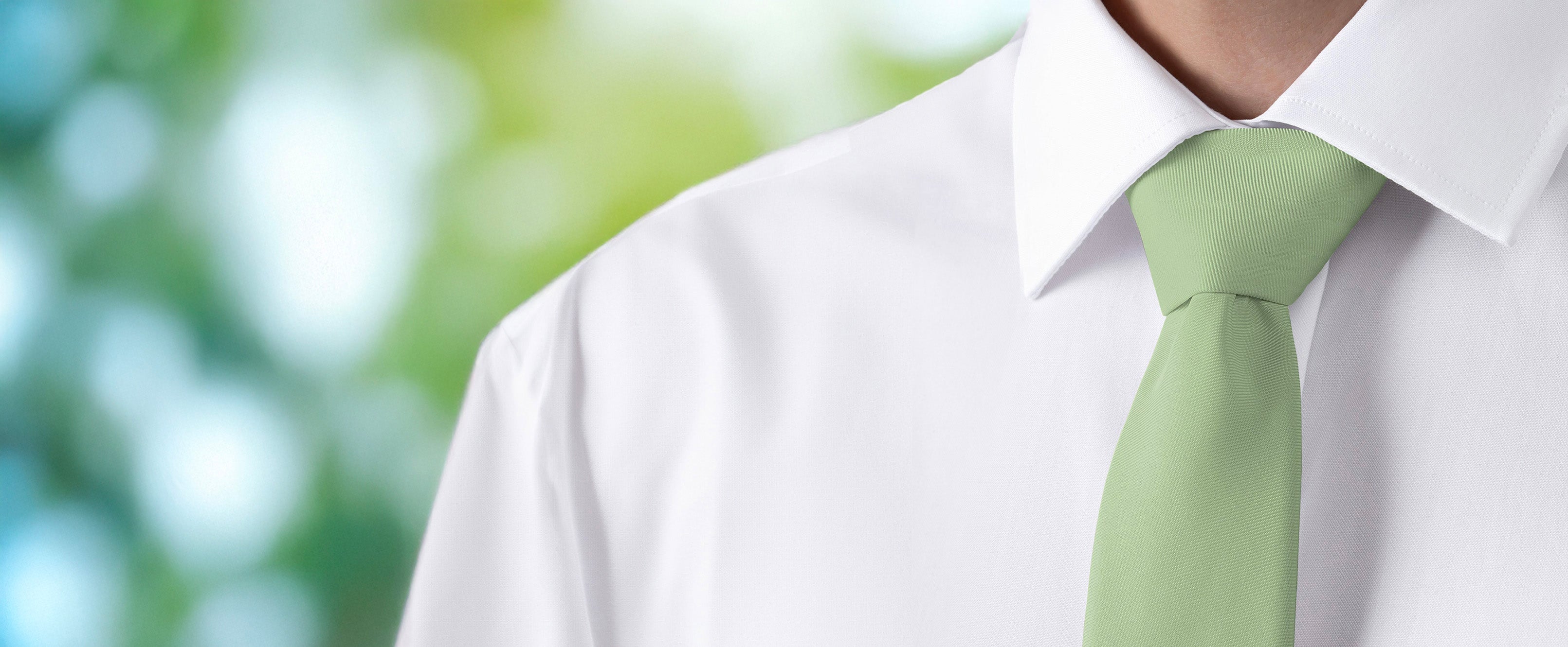 Light green solid color tie worn with a white shirt against a blurred natural background