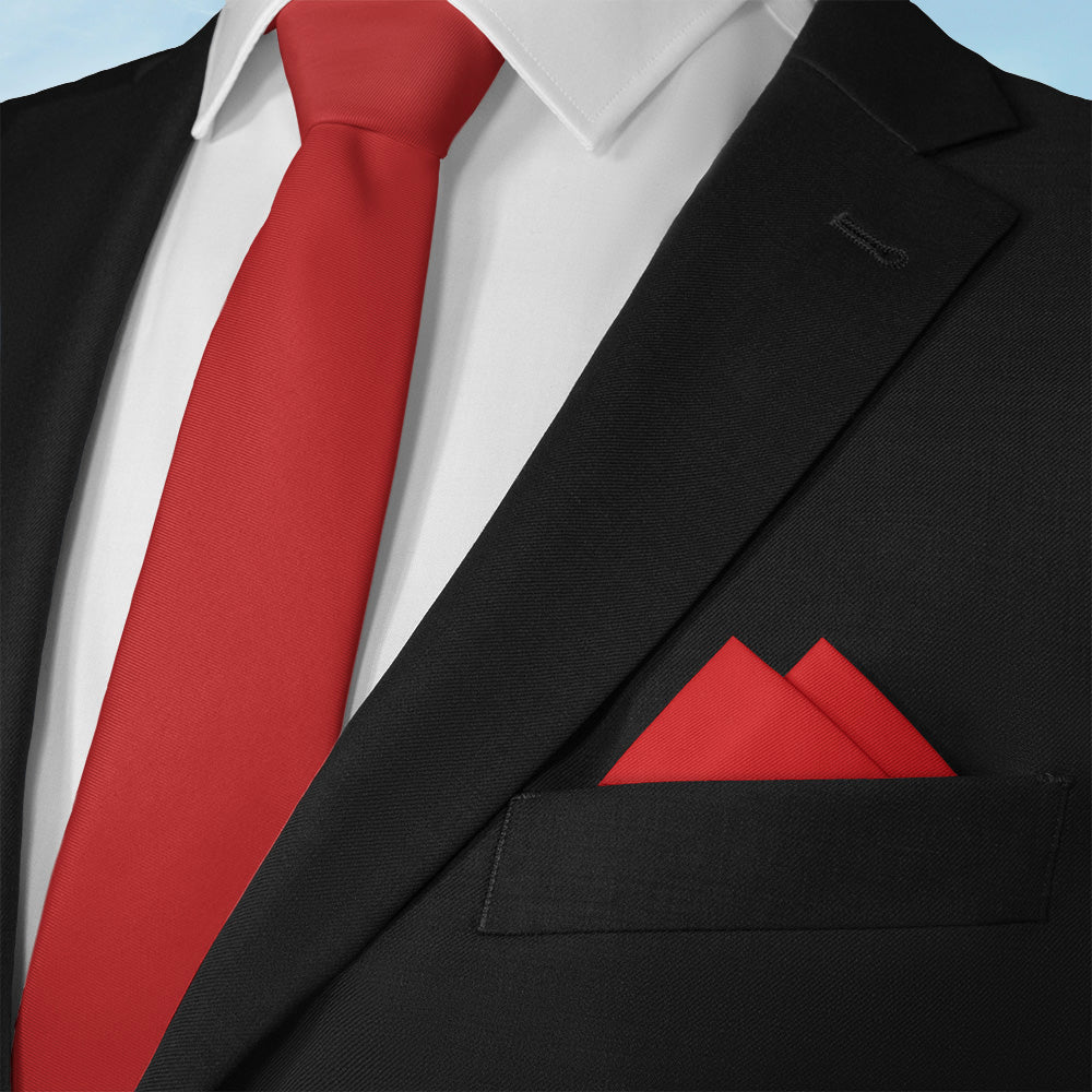 Black suit with a solid red tie and matching solid pocket square on a light blue background