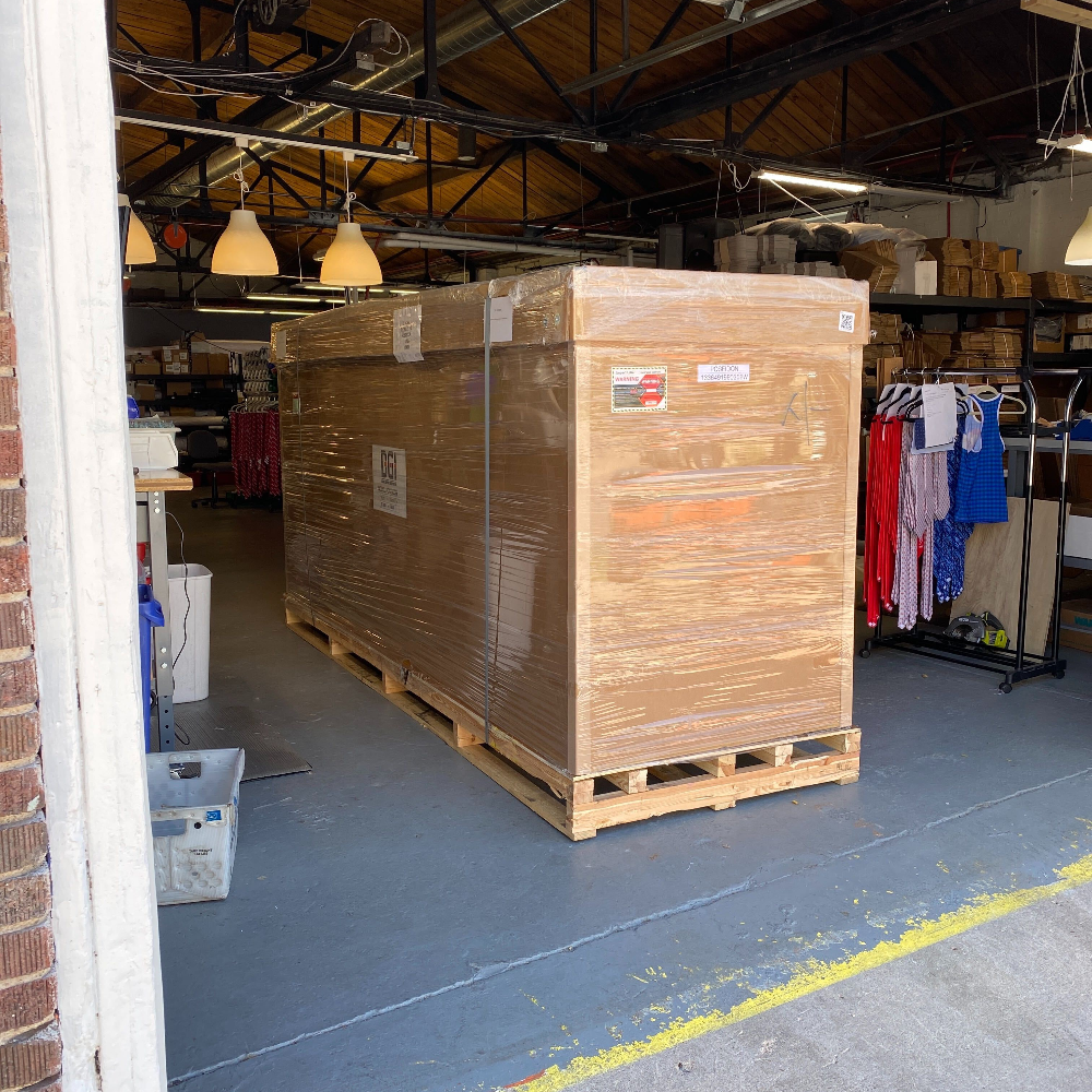 Large wooden crate on a pallet inside a warehouse with various items in the background.