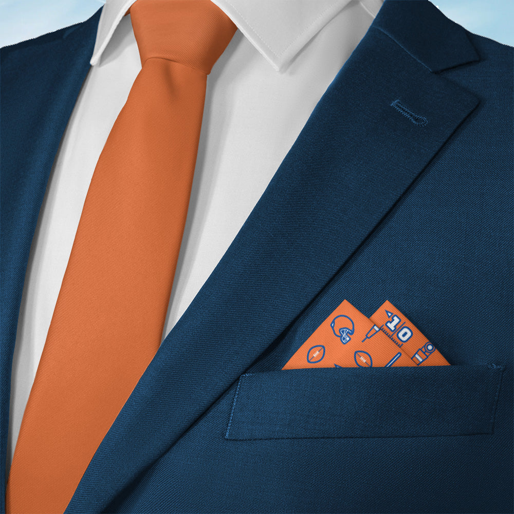 Navy suit with orange tie and matching sports themed pocket square on a light blue background