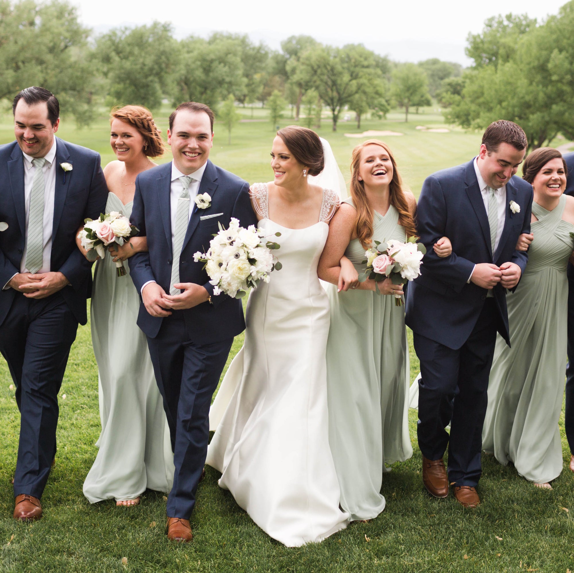 Bridal party linking arms and smiling on a golf course