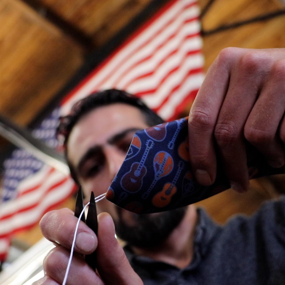 Person manufacturing  a necktie in front of an American flag