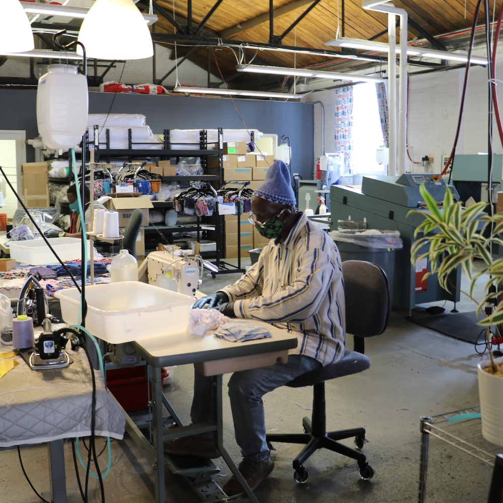 man sitting at a workstation preparing face masks in a warehouse setting