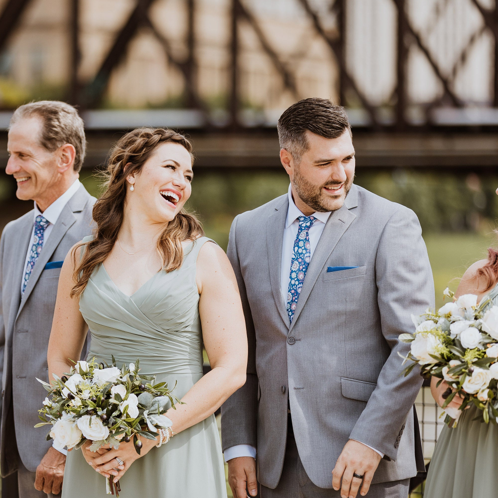 Group of people in formal attire with floral bouquets, standing outdoors.