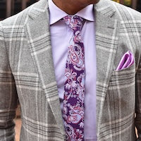 Person wearing a gray plaid blazer with a purple patterned tie and matching pocket square.