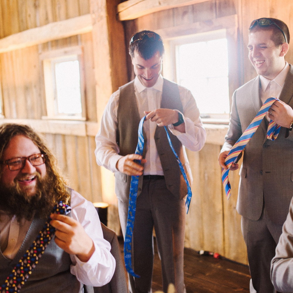 Three men in formal attire adjusting colorful ties in a wooden interior setting.
