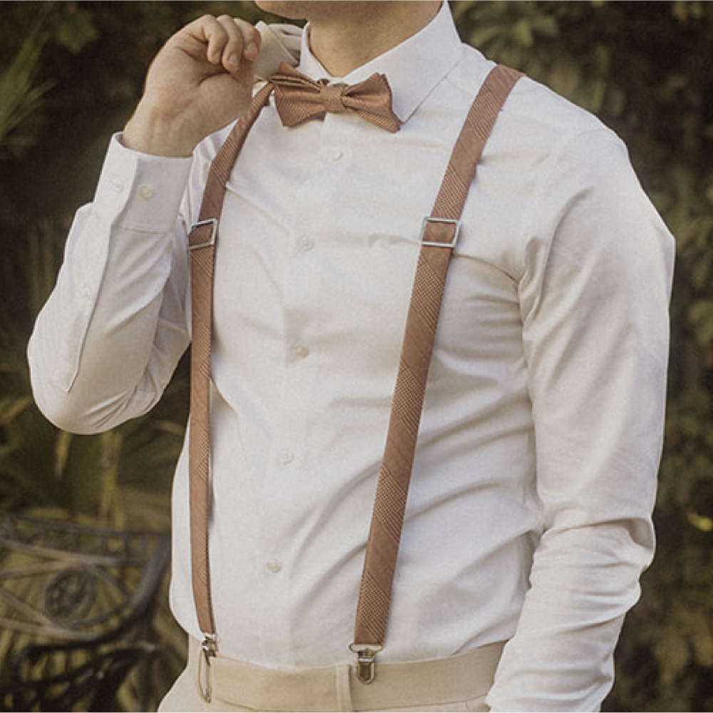 Person wearing a white shirt with brown suspenders and bow tie against a blurred natural background