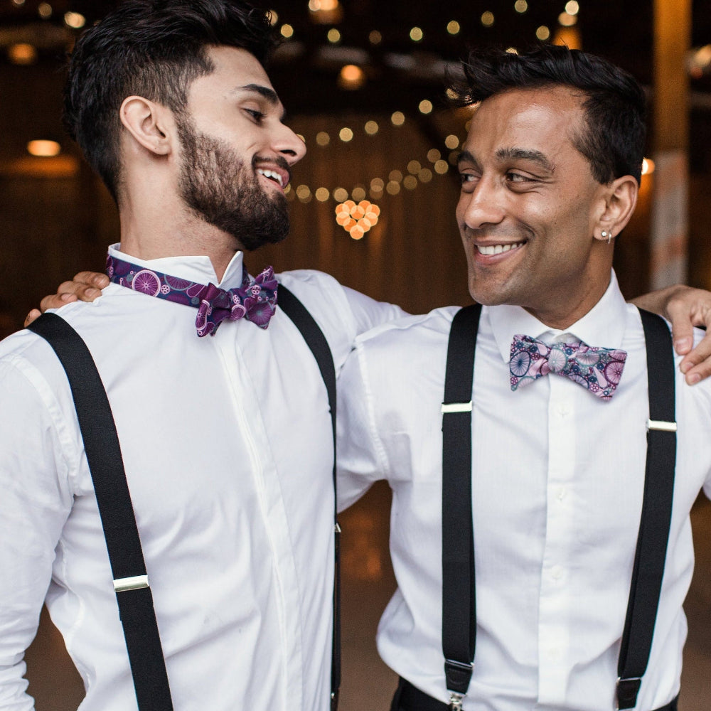 Two men wearing white shirts, black suspenders, and colorful bow ties.